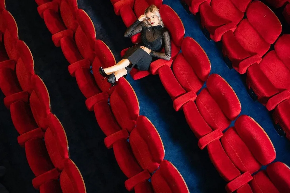 A fashion shoot in the auditorium, a model lying across the rows of red velvet